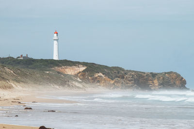 Lighthouse by sea against clear sky