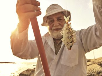 Portrait of mature man holding fish while standing at beach