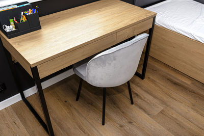 A wooden table with chair under the window in a modern boy room in black and white colors. 