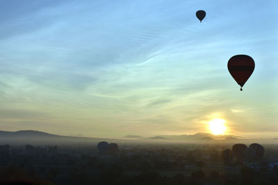 Hot air balloon flying over landscape against sky during sunset