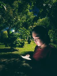 Woman reading book by tree against plants