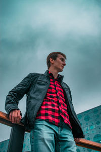 Low angle view of young man looking away against cloudy sky