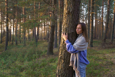 Unity with nature. young calm girl hugging pine tree trunk with closed eyes walking in autumn forest