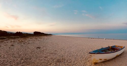 Boat moored on beach against sky during sunset