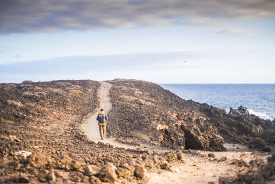 Rear view of mature man with backpack hiking on mountain by sea against sky