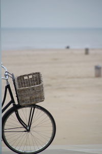 Bicycle leaning on beach by sea against sky