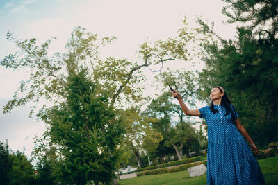 Low angle view of woman standing by tree against sky