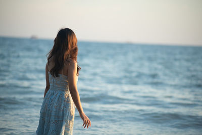 Rear view of woman standing by sea against sky