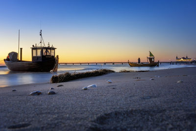 Sailboats moored on beach against clear sky at sunset