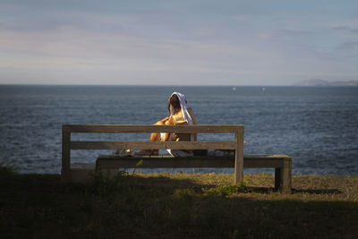 Rear view of man sitting on bench at beach
