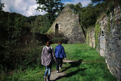 Rear view of two people walking in front of built structure