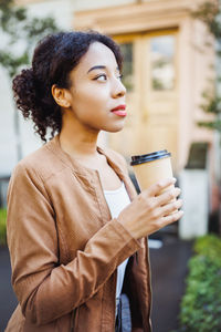 Young african mixed race woman holding disposable paper coffee cup on street