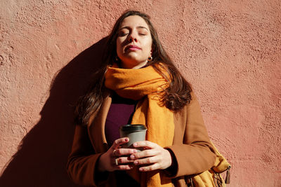 Beautiful young woman with coffee on wall