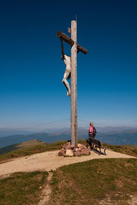 Woman standing by summit cross against blue sky