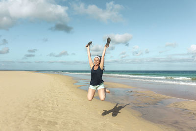 Smiling woman jumping with arms raised at beach