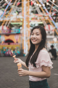 Portrait of smiling young woman holding bubble wand at amusement park