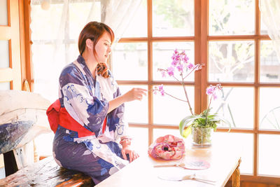 Young woman in kimono looking at orchid vase at home