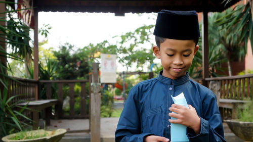 Smiling boy with envelope standing against plants