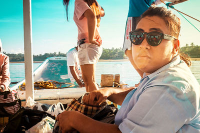 Portrait of young man wearing sunglasses sitting in boat on sea against sky