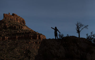 Low angle view of silhouette teenage girl standing on cliff against sky