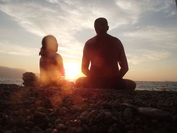 Father and daughter sitting at beach against sky during sunset