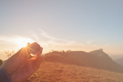 Cropped hand of person holding navigational compass against sky