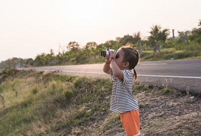 Rear view of woman photographing while standing on road