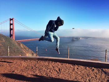 Full length of man jumping against clear blue sky