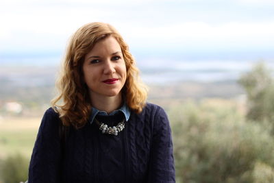 Portrait of smiling young woman standing on mountain against sky