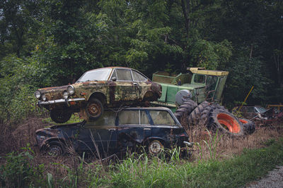 Abandoned cars in field. one stacked on the other. farm machinery in background. 