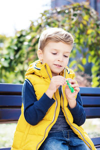 Boy holding yellow while sitting outdoors