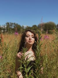Portrait of beautiful young woman amidst flowering plants on field against sky