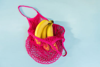 Yellow ripe bananas in a fuchsia eco cotton string bag on a pastel blue background