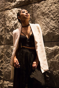 Young woman looking away while standing against wall