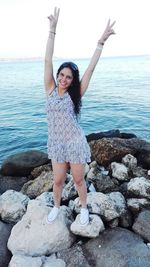 Full length portrait of woman standing on rock at sea shore