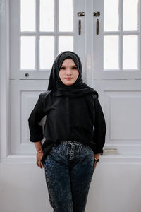 Portrait of young woman standing against wall