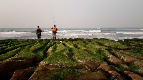 Men standing on beach against sky