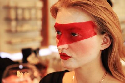 Close-up of young woman with red face paint looking away
