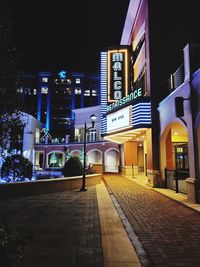 Illuminated street amidst buildings against sky at night