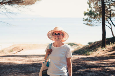 Portrait of smiling young woman wearing hat standing at beach