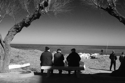 Rear view of people sitting on bench at beach