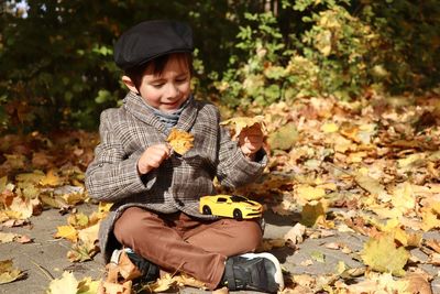 Cute boy holding leaf while sitting outdoors