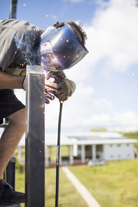 Close up view of man welding outdoors on rooftop.