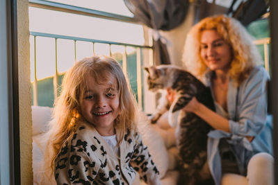 Happy child with smile plays on summer at home with mom, cat at sunset. cat, dog, pets family member