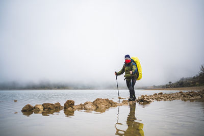 Man standing on rock by lake against sky