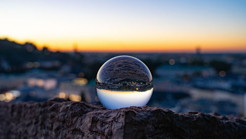 Close-up of crystal ball on rock against clear sky during sunset