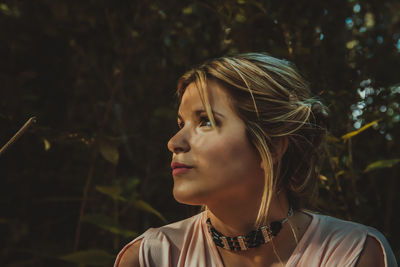 Young woman looking away against trees