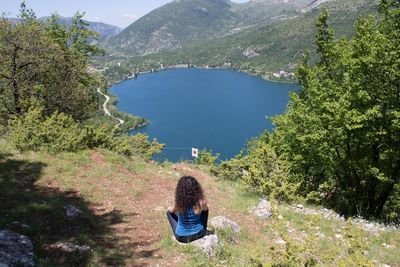 Rear view of woman sitting on mountain by lake