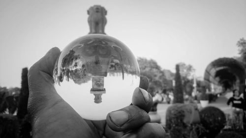 Close-up of hand holding crystal ball against sky