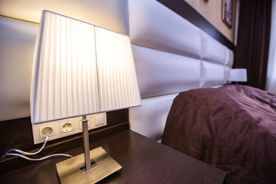 Illuminated electric lamp on side table in bedroom at home